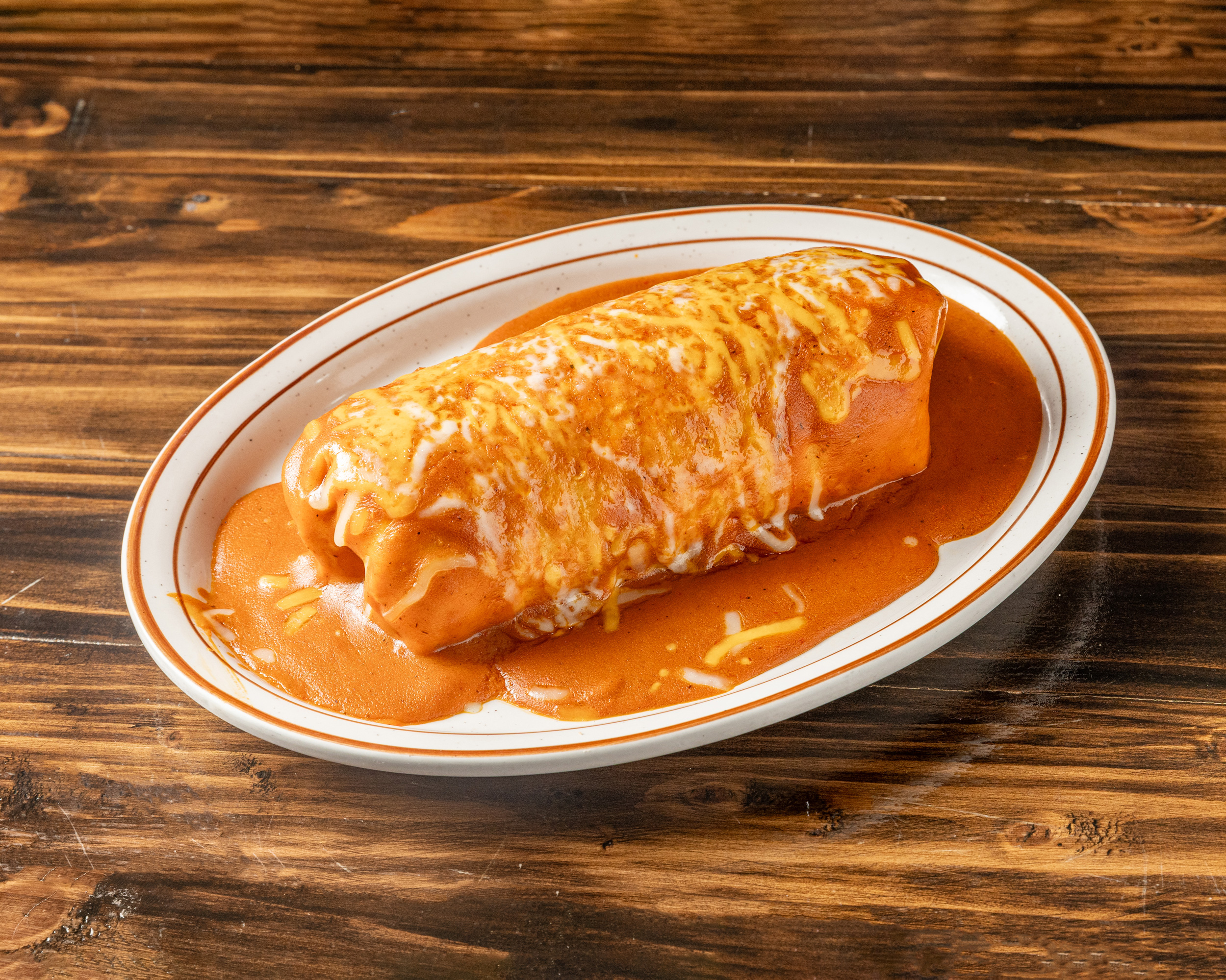 Smothered burrito topped with red sauce and melted cheese on an El Farolito Jr. plate